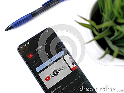 Modern workspace with smartphone with YouTube Kids app play store page on white background Editorial Stock Photo