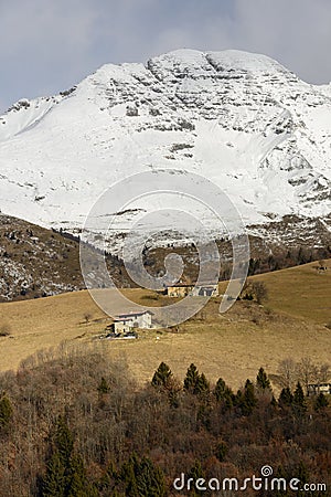 Lodges in glades under snowy rocky slopes of Arera peak, Italy Stock Photo