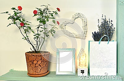 Paper bag with lavender flowers, rose plant in pot, picture frame on wooden shelf. Stock Photo