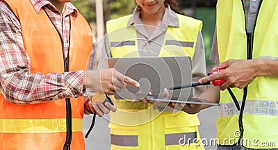 Logistics engineering team analyzing data on a tablet and discussing project metrics on-site Stock Photo