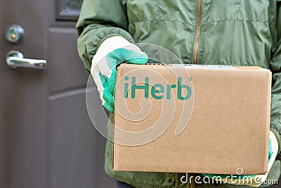 Logo iHerb on cardboard box in courier hands. iHerb is an herbal products company Editorial Stock Photo