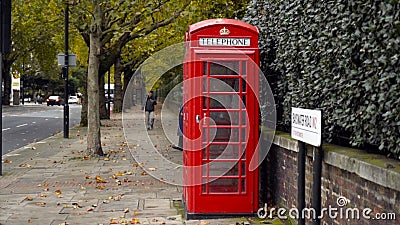 London, Britain-September, 2019: Red telephone booth on street with trees and people. Action. Red public telephone booth Editorial Stock Photo