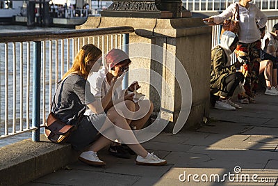 London, U.K., August 22, 2019 - Two candid colleagues take a break sitting on the embankment eating near London Bridge by the Editorial Stock Photo