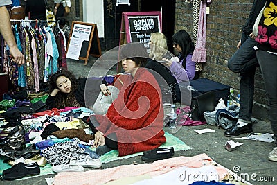 A two young fashionable girls friend sells their old things, sitting on the pavement in Bricklane at a Sunday street flea market Editorial Stock Photo