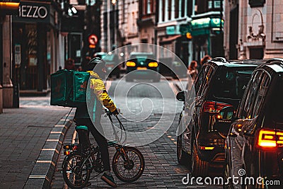 London UK February 2021 Lone Deliveroo food delivery man trying to make his way on a bicycle through a traffic jam, pushing his Editorial Stock Photo