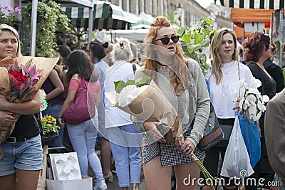 Red-haired girl in jeans shorts bought a bouquet of white hydrangea. Her friend is carrying a bouquet of orchids Editorial Stock Photo