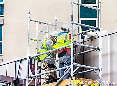 Two builders in retro-reflective clothing and helmets on scaffolding are engaged in repair work Editorial Stock Photo