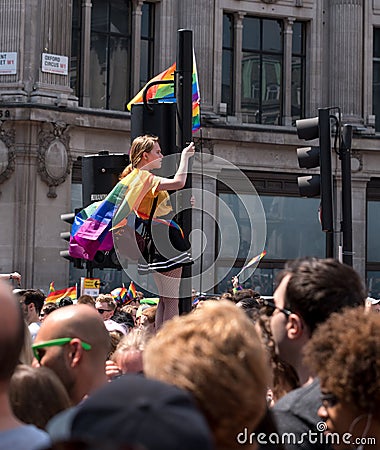 Woman with LGBT rainbow climbs up the traffic light pole at Oxford Circus to get a better view of the Gay Pride Parade. Editorial Stock Photo