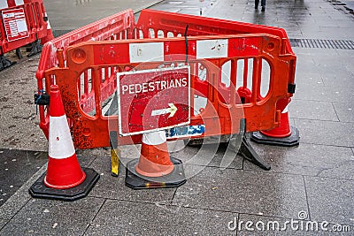 London, United Kingdom - February 04, 2019: Red roadblock with arrow sign directing pedestrians to walk around, placed on wet Editorial Stock Photo