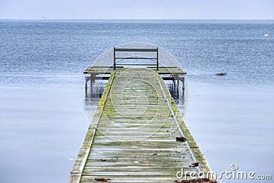 Lone bench facing a melancholic Baltic Sea on a fragile boardwalk conveys isolation, sadness and melancholy feelings. Dragor Stock Photo