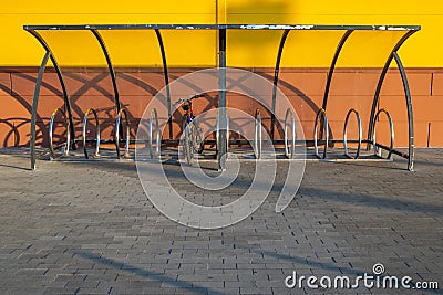 A lone bicycle standing in a bicycle parking near the yellow wall on a sunny summer day Stock Photo