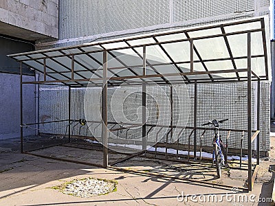 A lone bicycle stands in an indoor bicycle parking area near a gray concrete building on a sunny winter day Stock Photo