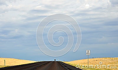 Lone biker on an empty rural road with `Do Not Pass` sign in the foreground Stock Photo