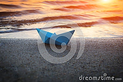 Lone blue paper boat washed up on the sandy beach at sunset Stock Photo