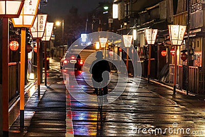 Lone cyclist and taxi on lantern lined road through Kyoto after rain Stock Photo