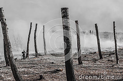 Lone firefighter in a field near a forest in smoke after putting out a fire Stock Photo