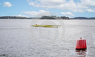 Lone fisherman fishing off isolated spit of land near to red market buoy in middle of Poole Harbour, Poole, Dorset, UK Editorial Stock Photo