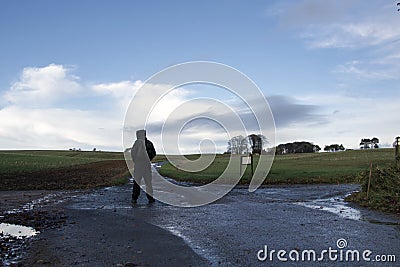 A lone hooded hiker with a rucksack standing at a crossroads on a winters day in the countryside Stock Photo