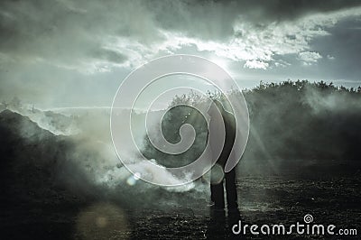 A lone hooded silhouetted figure standing outside. In a burnt smoking landscape. With a high contrast edit. With deliberate lens f Stock Photo