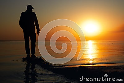 A lone man stands on the seashore during dawn. Beautiful view of the sea and the sun Stock Photo