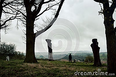 A lone moody hooded figure standing on a hillside, looking out across the English countryside in winter Stock Photo