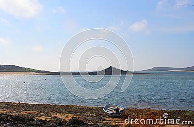 A lone boat waits on the weedy shore by the empty waters off Tresco island in the Isles of Scilly England. Stock Photo