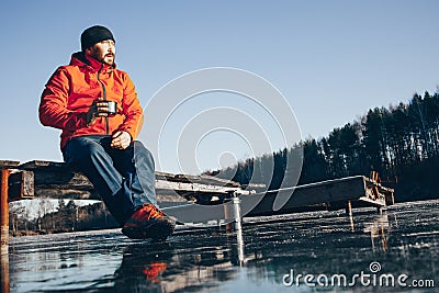 A lone tramp traveler stands on ice and drinks tea from a thermos. Stock Photo