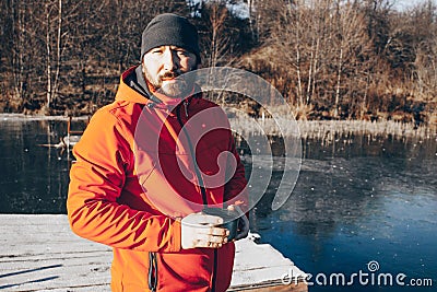 A lone tramp traveler stands on ice and drinks tea from a thermos. Stock Photo