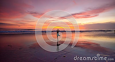 A lone woman doing yoga on a beach at sunset Stock Photo