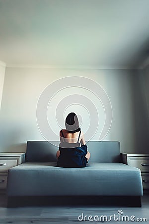 Loneliness. Alienation. Girl in an empty room sits back on a couch and looks in the wall Stock Photo