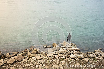 Lonely Asian fisherman standing on rocks in front of water Editorial Stock Photo