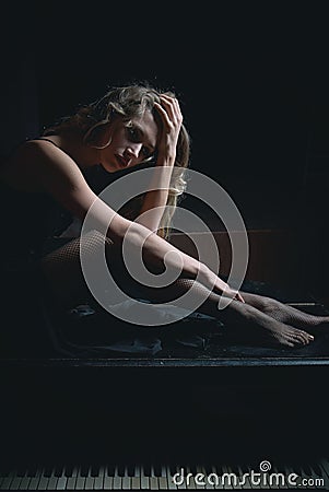 Sad beautiful girl sitting on black piano in the dark room Stock Photo
