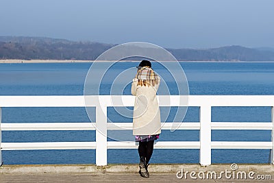 Lonely beautiful sad girl is standing on the pier on a sunny warm autumn evening at the sea Stock Photo