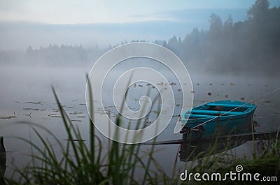 Lonely boat on a peaceful lake. Foggy autumn sunrise twilight. Bright blue turquoise shallop quiet forest, swamp plants Stock Photo