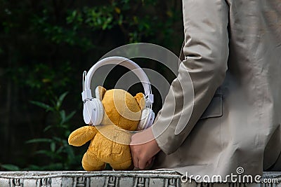 Lonely boy sitting, with his teddy bear in the park. Teddy bear toy wearing headphones and listening music in holida Stock Photo