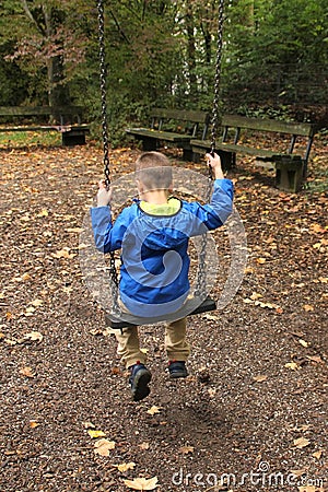 Lonely child in a blue jacket sits on a swing in a park in an autumn park, the concept of loneliness Stock Photo