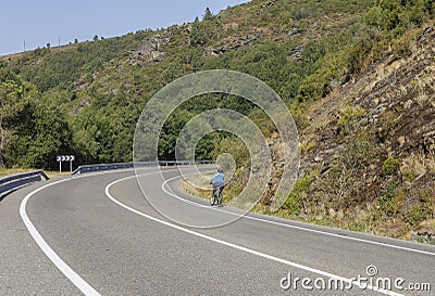 A lonely cyclist biking in an empty spanish road during the summer, Triacastela, Galicia, Spain. Editorial Stock Photo