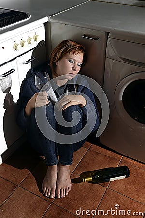 Lonely drunk alcoholic woman sitting on kitchen floor in depression drinking wine Stock Photo