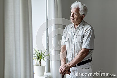 Lonely elderly man with walking stick standing by the window alo Stock Photo