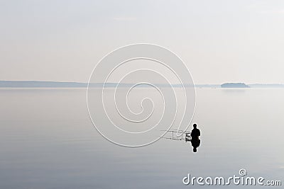 Lonely fisherman on the lake in the morning light Stock Photo