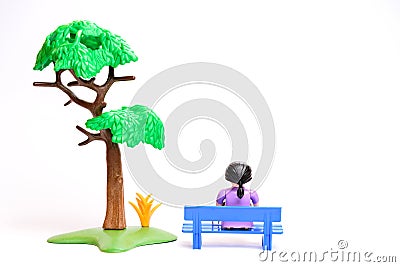 Lonely girl sits on a bench near a tree children's figurines toys Stock Photo