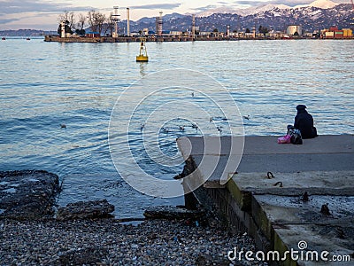 A lonely girl sits on a pier in the port. Sitting on the edge of the water Stock Photo