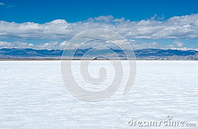 Lonely glittery white salt flat with a road and trucks on the horizon Stock Photo