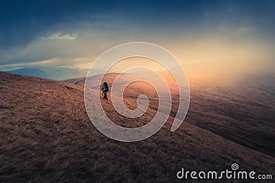 Lonely hiker with backpack walking along the trail on the mountain top at foggy day time. Stock Photo
