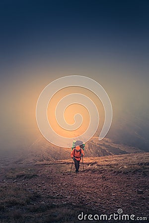 Lonely hiker with backpack walking along the trail on the mountain top at foggy day time. Stock Photo