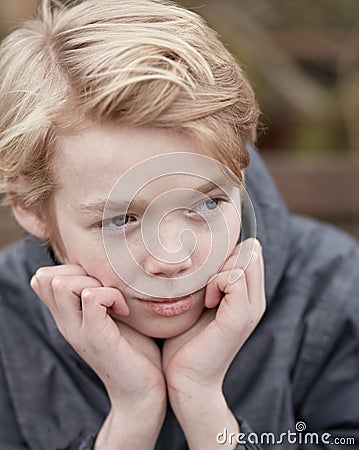 Lonely kid with his hands on his chin thinking. Young little teen kid outside on a playground alone. Cute caucasian male Stock Photo