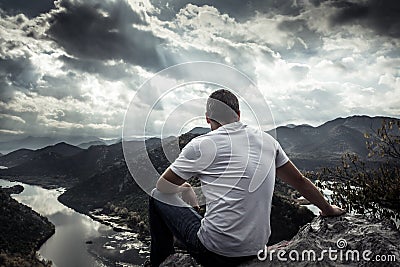 Lonely man looking with hope at horizon on mountain peak with dramatic sunlight during sunset with effect of light at the end of t Stock Photo