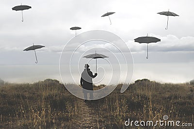 Lonely man with umbrella walks down a road towards the lake and surreal black umbrellas fly in the sky Stock Photo