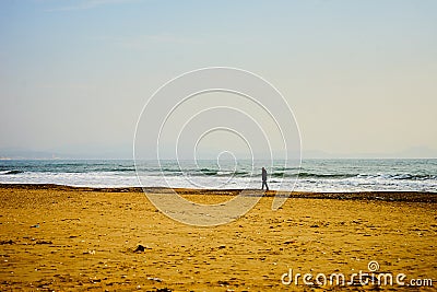 A lonely man wanders along a deserted sandy beach. Stock Photo