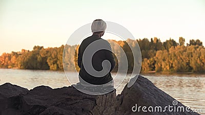 Lonely old woman sitting near lake and throwing stones solitude, back view Stock Photo